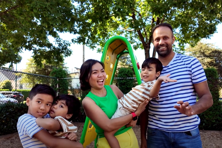 parents with three little boys pose smiling for a picture in a playground
