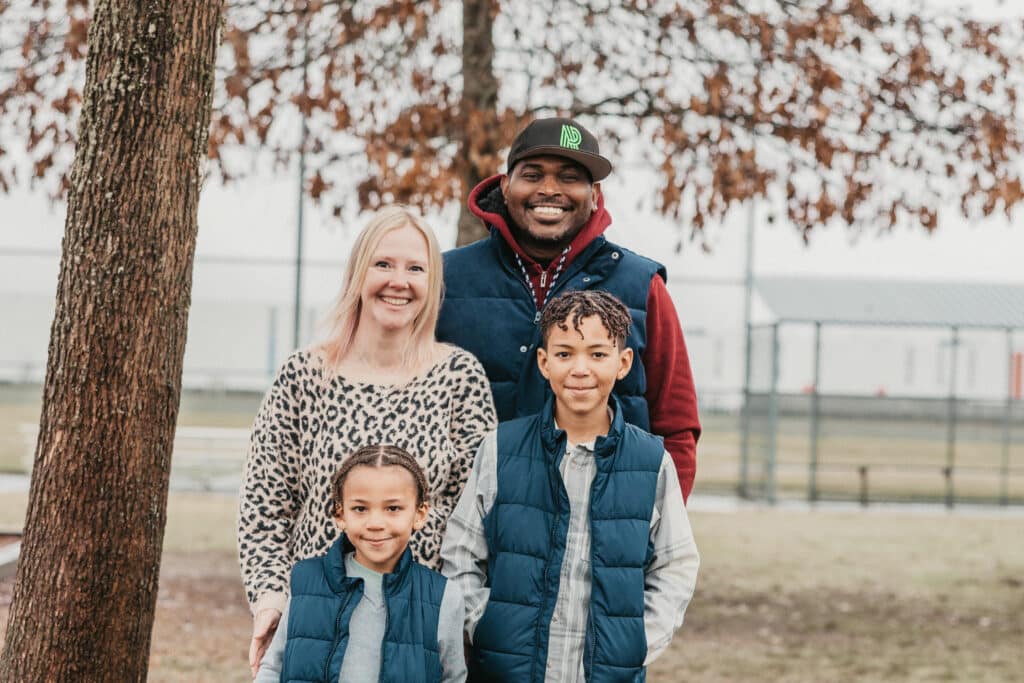 Mehkai and parents and brother pose smiling in a park.